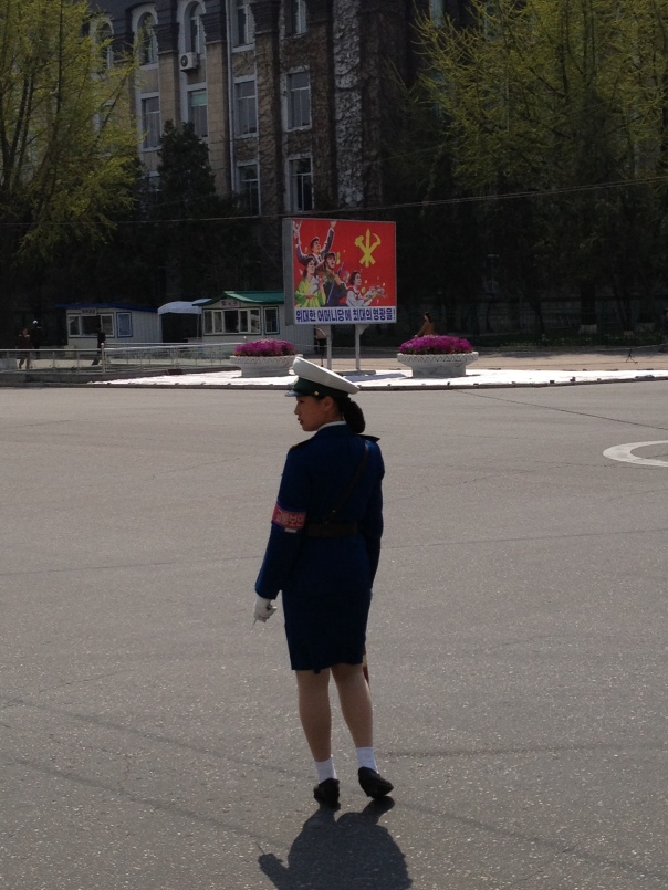 A traffic lady stands across from a party propaganda poster, the only sort of street art you'll find in Pyongyang